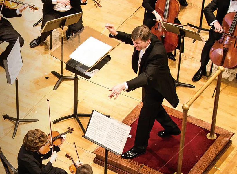 Symphony orchestra conductor directing musicians during formal concert performance